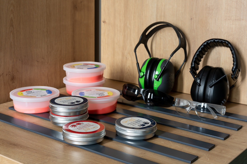 Półka w pokoju wyciszenia. Dwie pary słuchawek wyciszających – mniejsze i większe, dwie pary okularów – ciemne i jasne. Obok kilka pudełek z różnego rodzaju masami sensorycznymi.