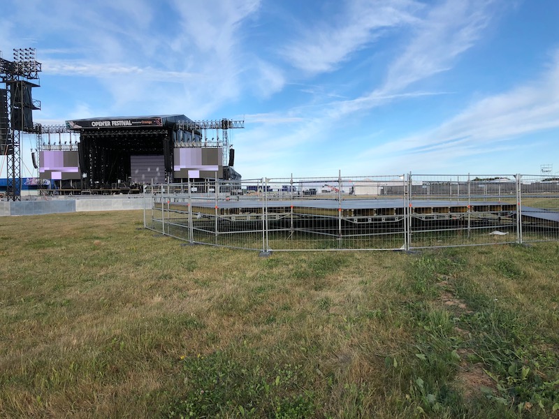 Teren festiwalu plenerowego. W odległości kilkudziesięciu metrów od sceny rozstawiona strefa dostępna - ogrodzona podwyższona platforma. Do niej prowadzi rampa.