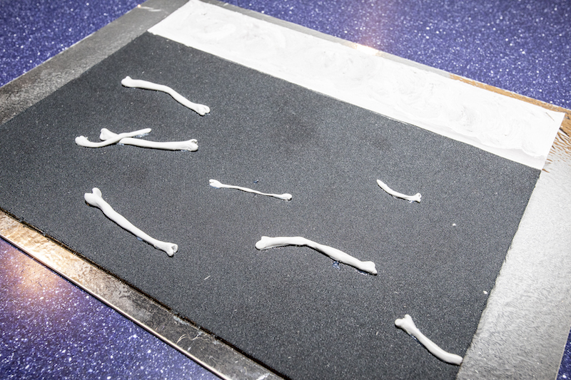 Tyflografika obrazu. Niebo namalowane gładką farbą, tafla wody to miękka gąbka, pośrodku unoszące się kości wykonane z modeliny.