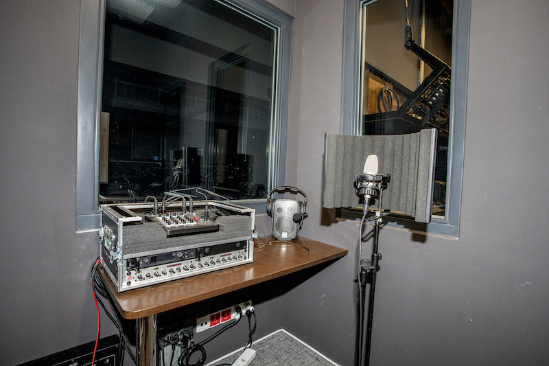 Wnętrze kabiny. Niewielkie pomieszczenie, ściany pomalowane na czarno, pośrodku ustawiony stół, na nim sprzęt do regulowania dźwięku, obok mikrofon, głośnik, słuchawki. Nad stołem okno z widokiem na scenę.